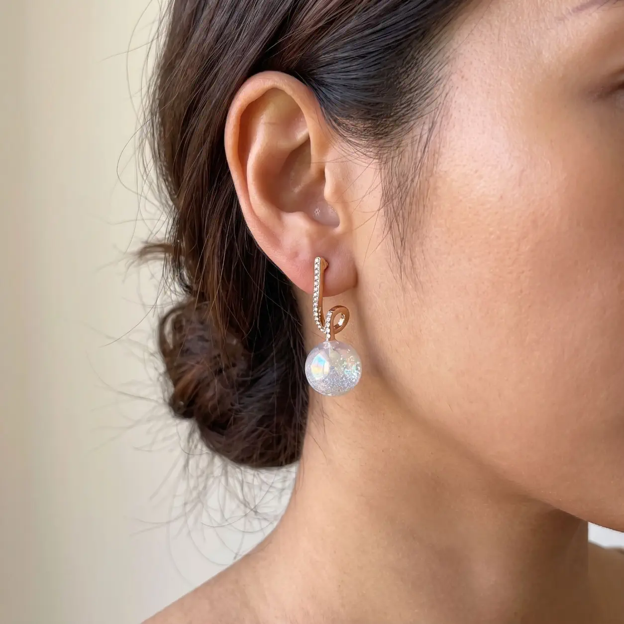 نمای نزدیک گوشواره طلایی نگین‌دار با آویز گوی شفاف اکلیلی